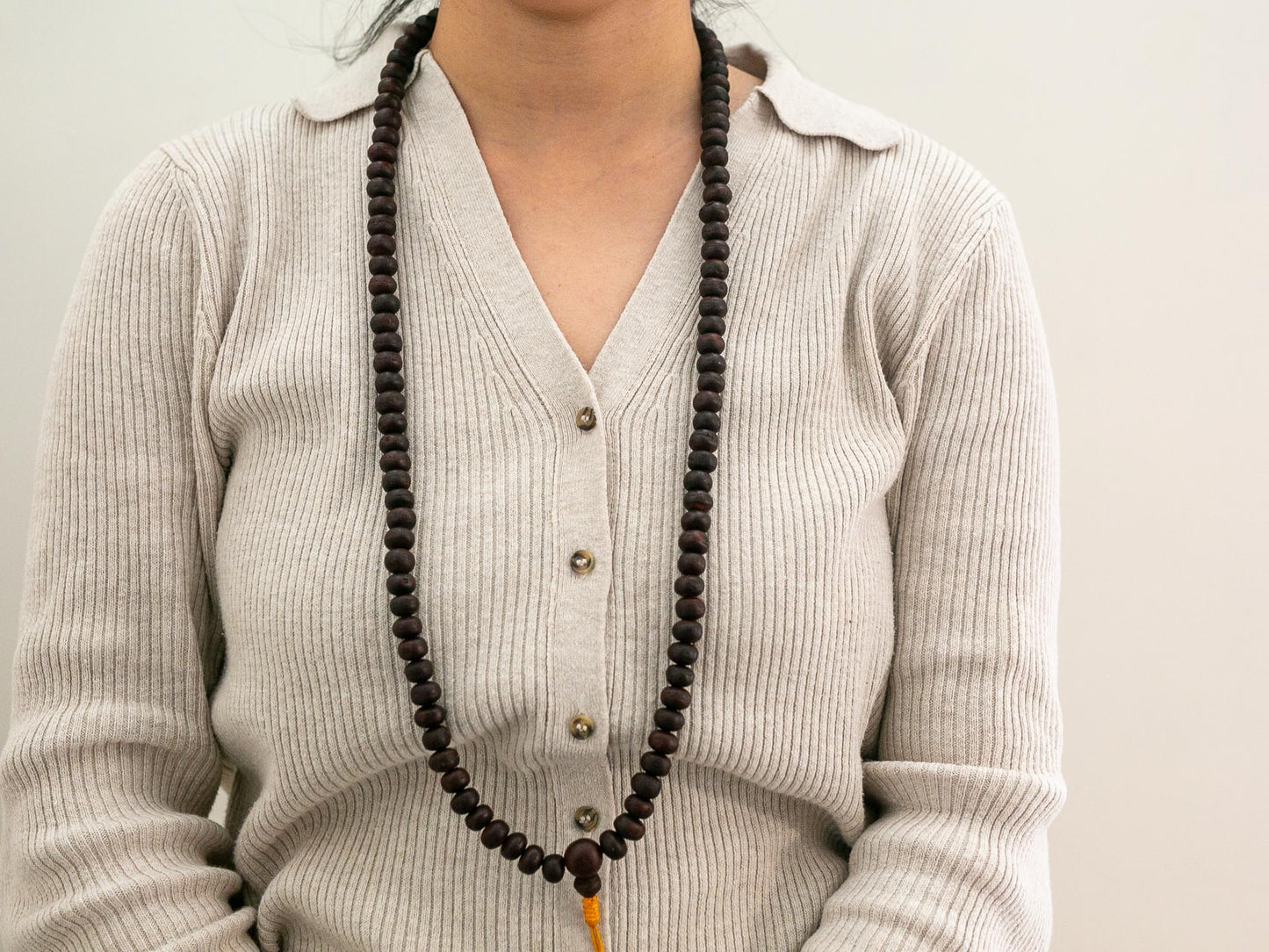 Person wearing a long dark Bodhi mala beaded necklace with a light gray sweater.