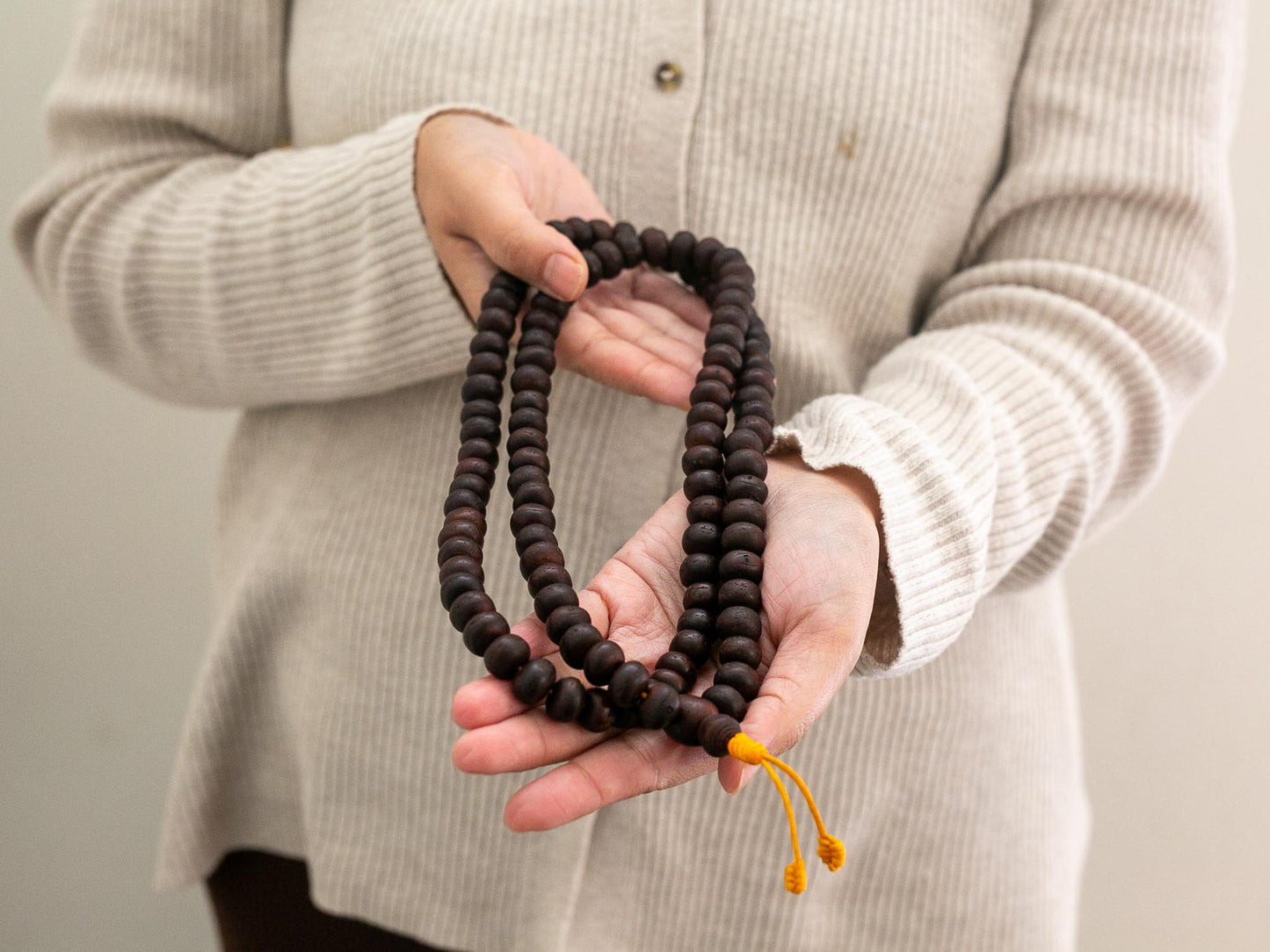 Person holding a set of brown Bodhi mala prayer beads with a beige background