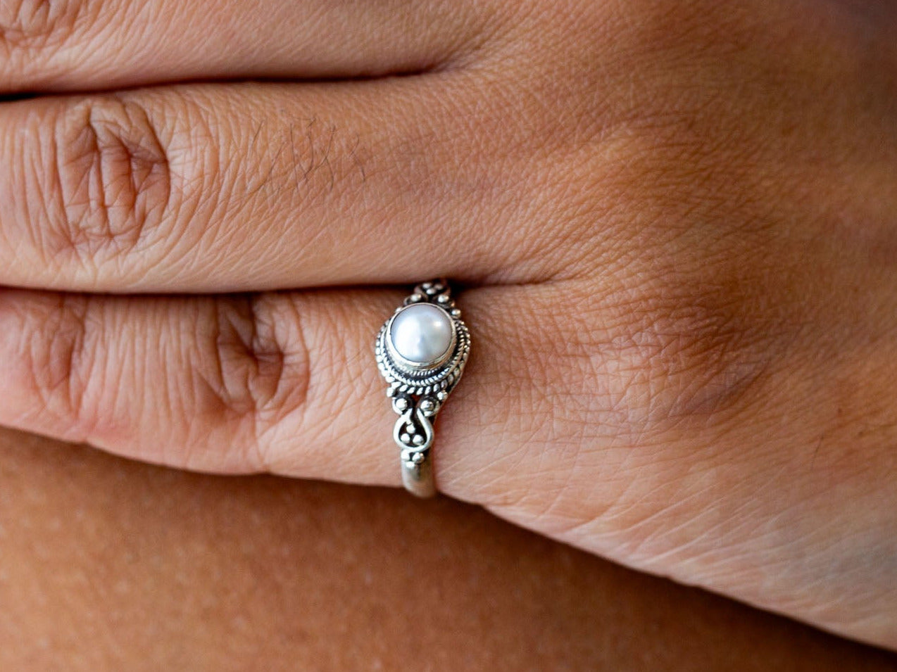 Close-up of a hand wearing a silver ring with a pearl on a blurred background