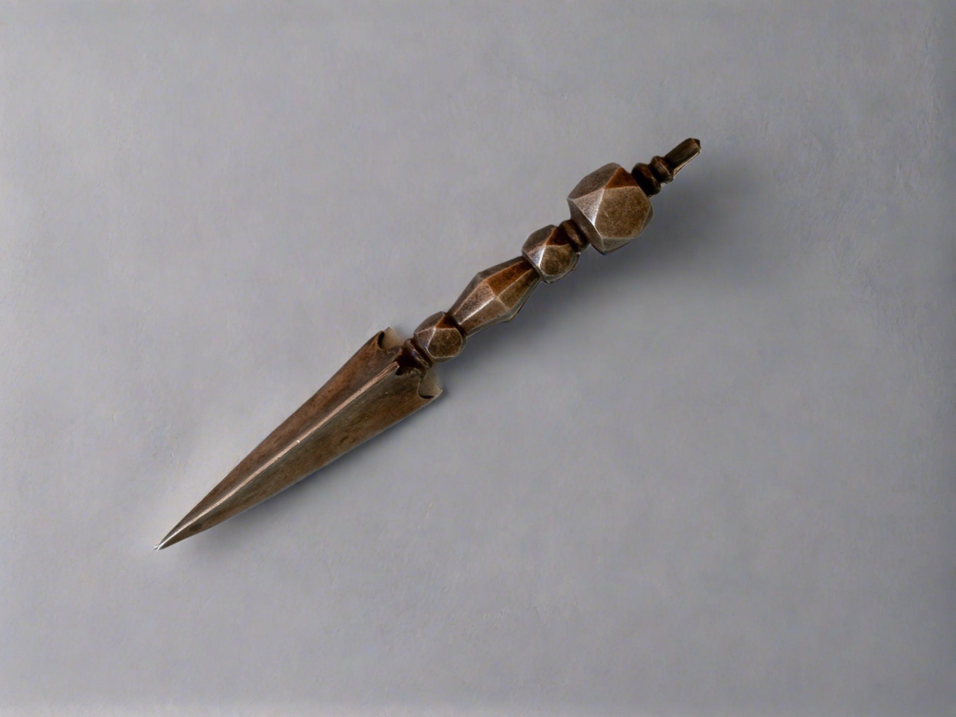 iron phurba dagger viewed sideways against grey backdrop
