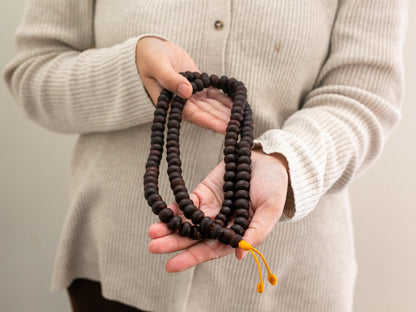 Person holding a set of brown Bodhi mala prayer beads with a beige background