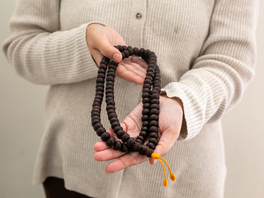 Person holding a set of brown Bodhi mala prayer beads with a beige background