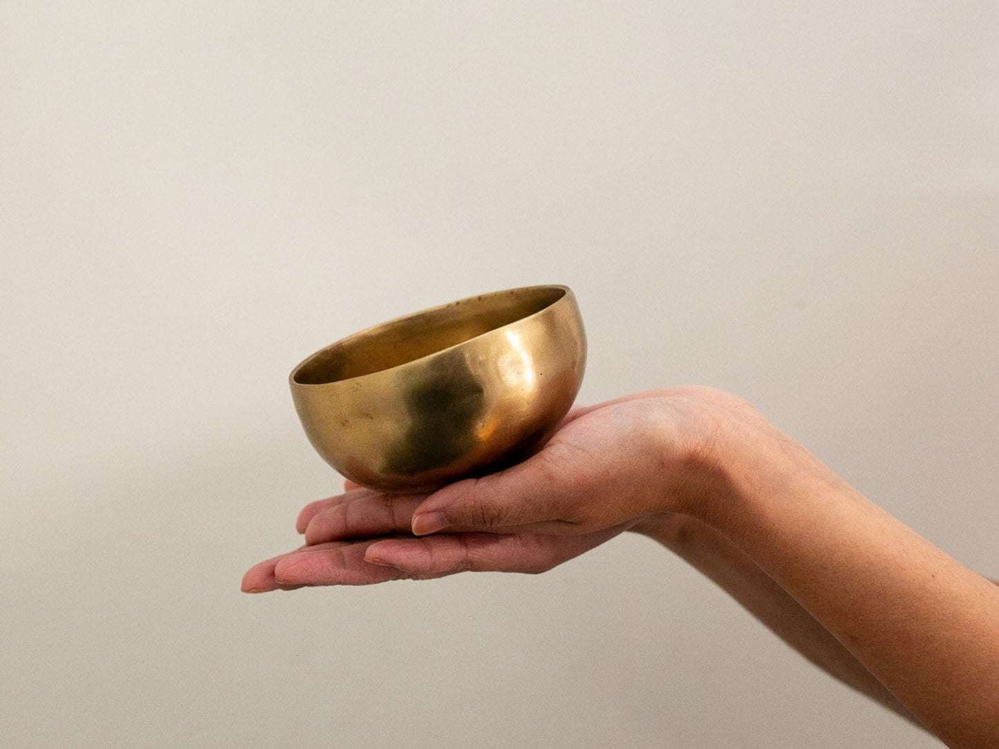Hand holding a brass bowl against a plain background