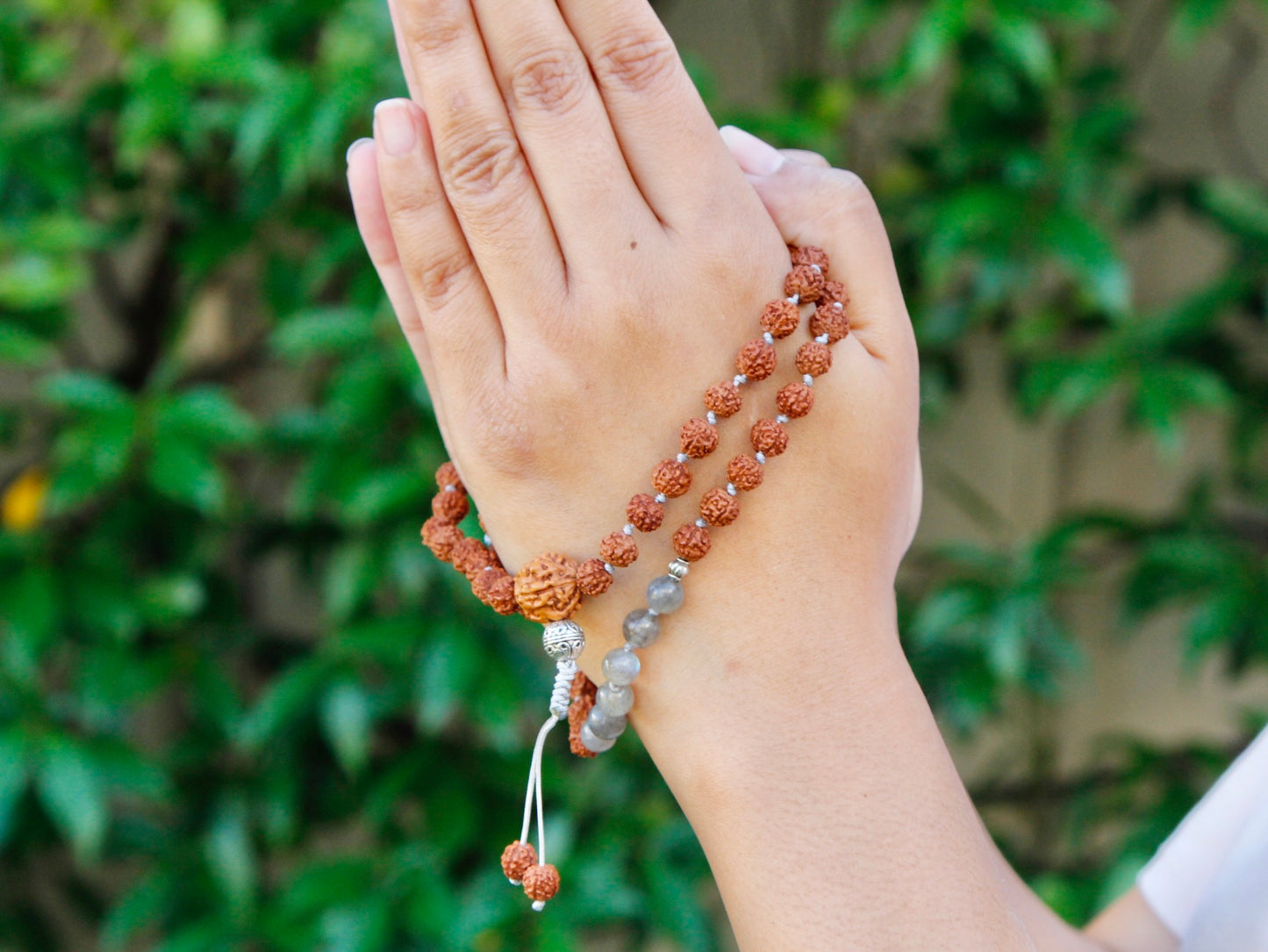 Rudraksha mala wrapped around hand in namaste gesture