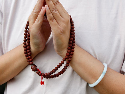 Dark rakhtu seed mala in hands folded in Namaste gesture
