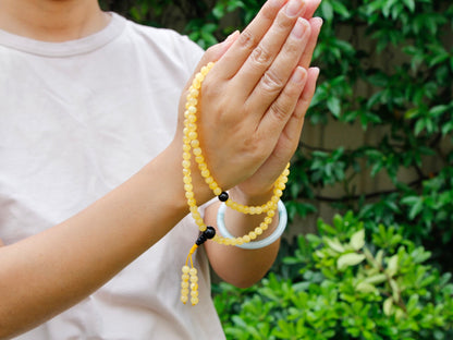 Amber mala held between hands in Namaste gesture